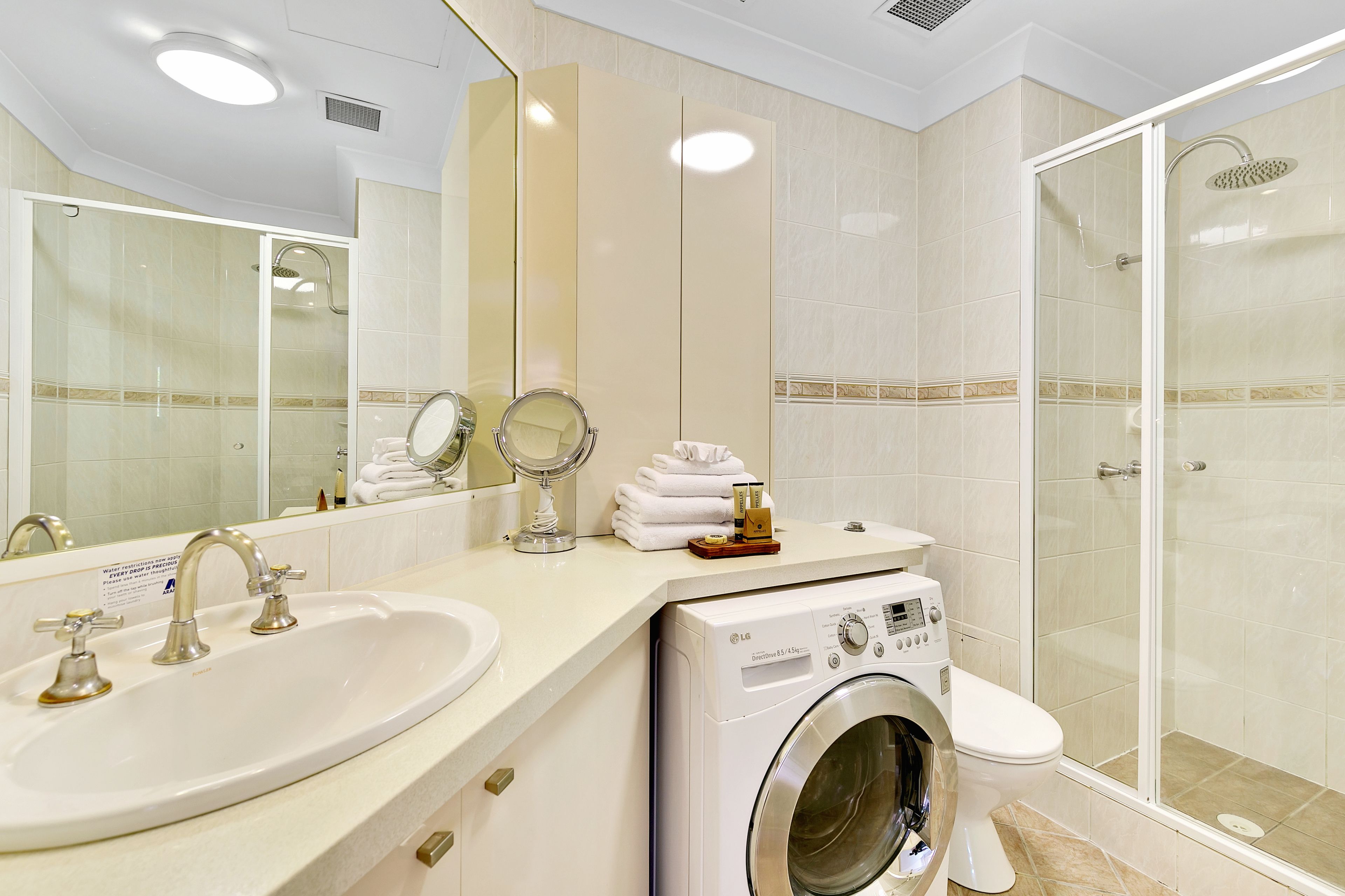 Ein Hotelbad mit Waschbecken, Spiegel, Handtuchhalter, Waschmaschine, Toilette und einer Duschkabine.