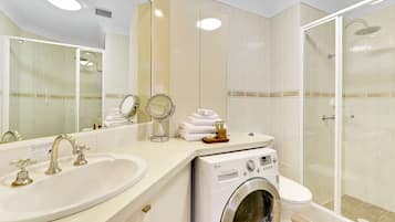 Ein Hotelbad mit Waschbecken, Spiegel, Handtuchhalter, Waschmaschine, Toilette und einer Duschkabine.