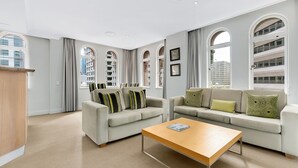 Una sala de estar moderna con un sofá color beige, una mesa de centro de madera y amplias ventanas arqueadas con cortinas.