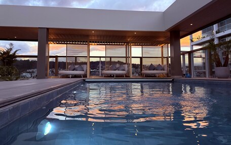 A rooftop pool area with lounge chairs and a view of the city skyline at sunset.