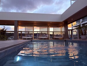 Un área de piscina en la azotea con sillones de descanso y vistas al horizonte urbano al atardecer.