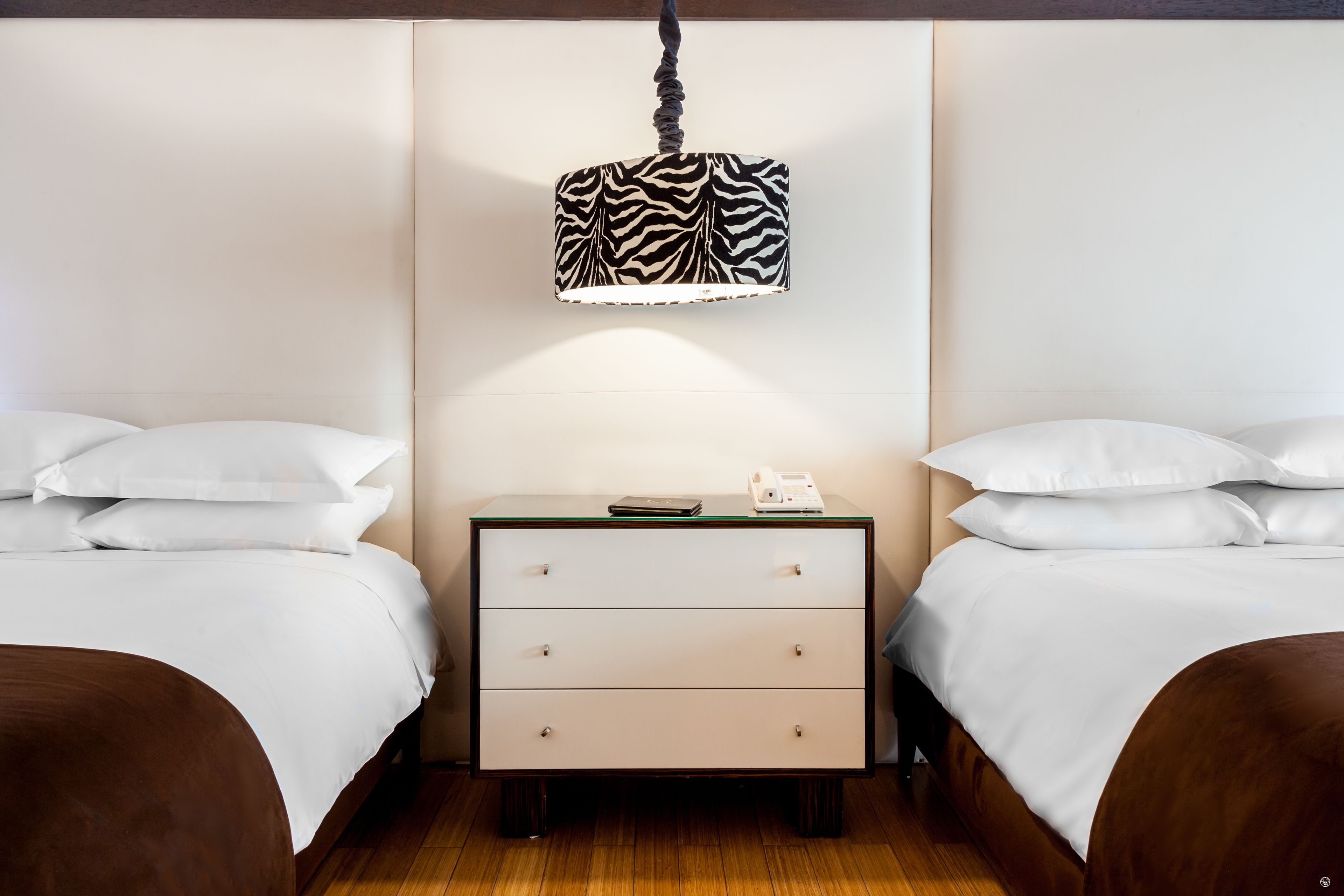 A hotel room with two beds, a bedside table with a telephone, and a zebra-patterned lamp.