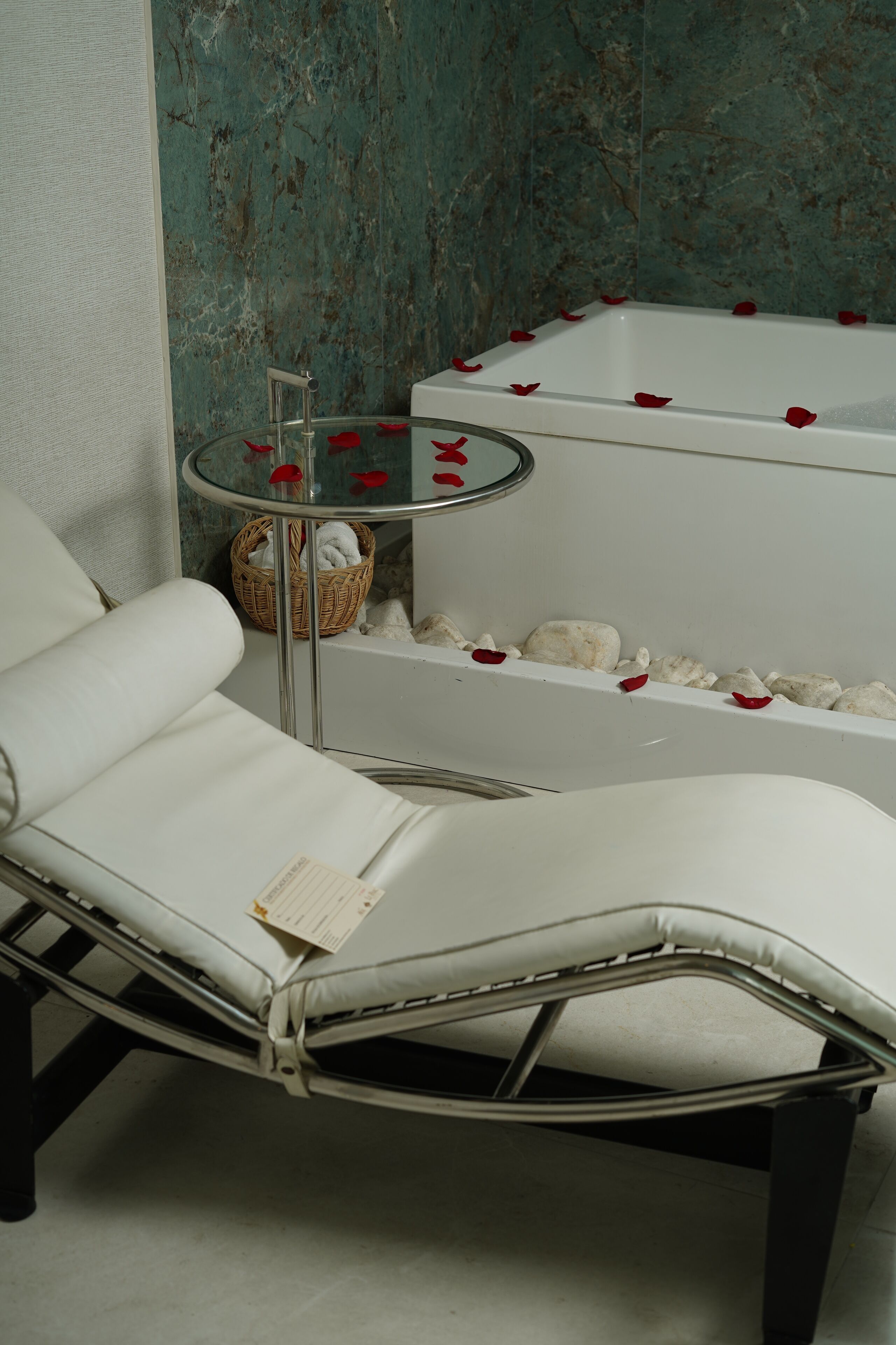 A modern bathroom with a glass-topped bathtub, a white cushioned chair, and a small wicker basket.