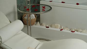 A modern bathroom with a glass-topped bathtub, a white cushioned chair, and a small wicker basket.