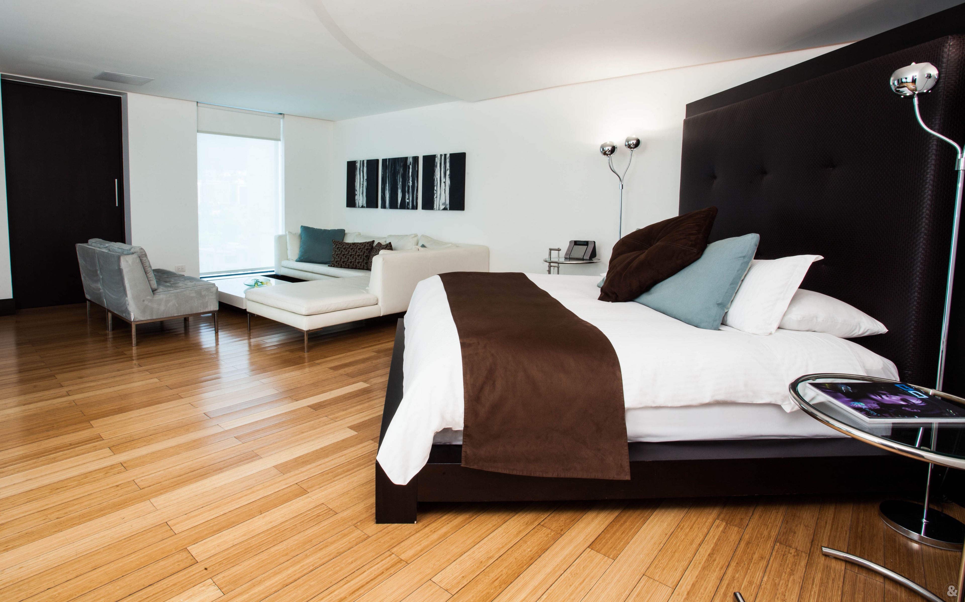 A modern hotel room with a large bed, a sofa, a chair, and a desk.