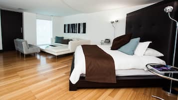 A modern hotel room with a large bed, a sofa, a chair, and a desk.
