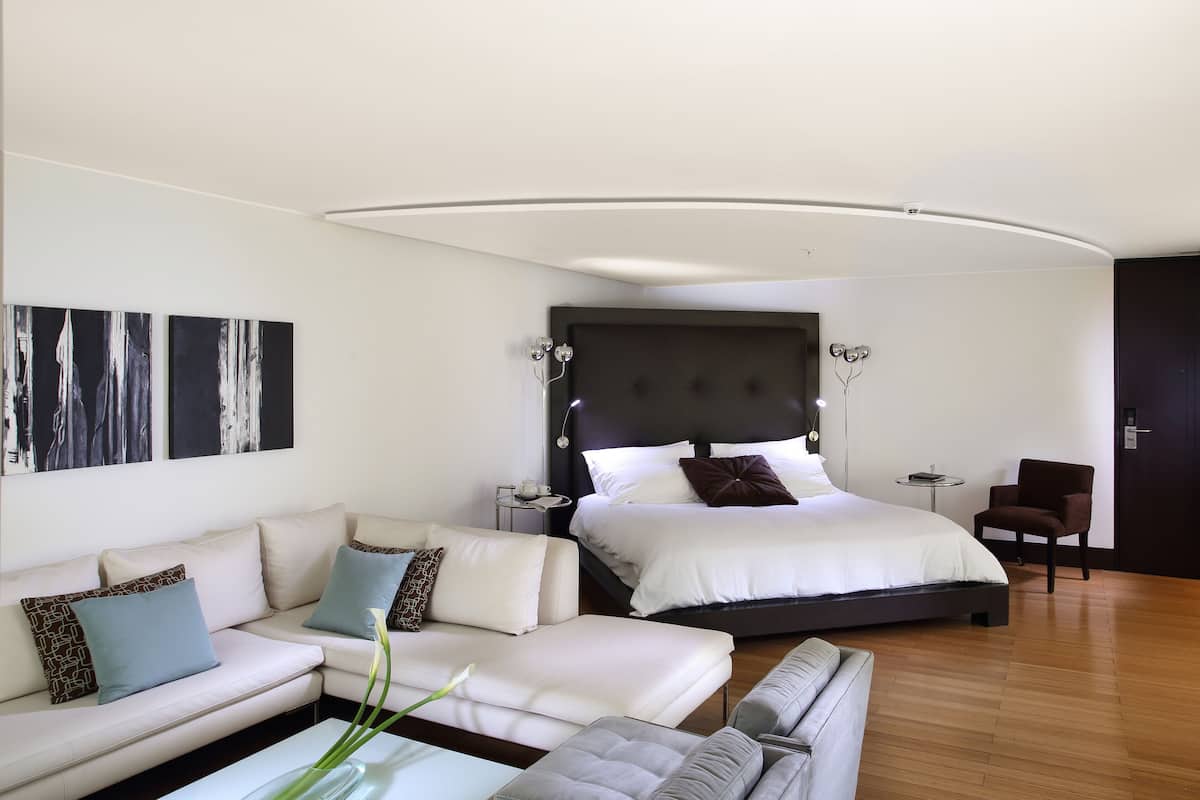 Una habitación de hotel moderna con una cama grande, un sofá, una mesita y una silla.