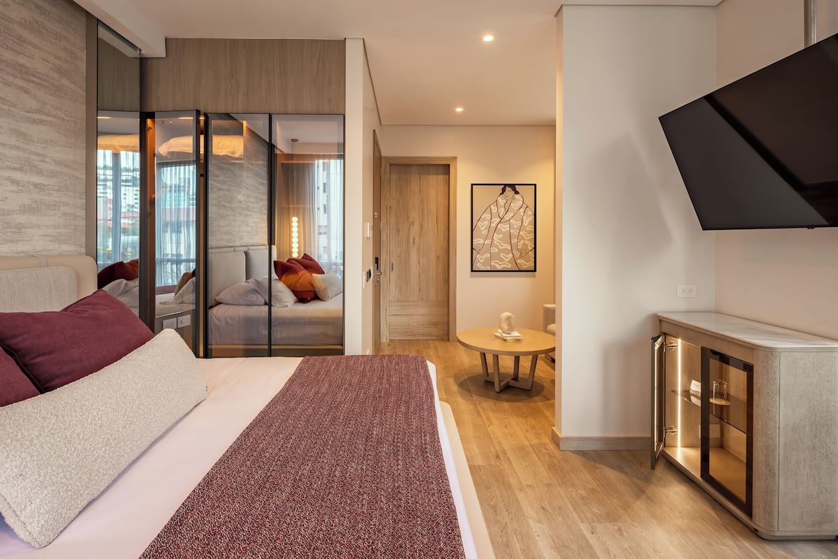 Una habitación de hotel moderna con cama, zona de estar con vistas, una mesita y televisor montado en la pared.