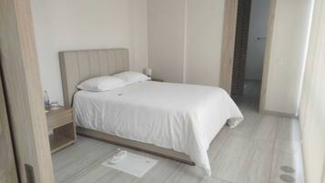 Une chambre à coucher bien rangée, avec un lit, une table de chevet et une porte donnant sur une autre pièce.
