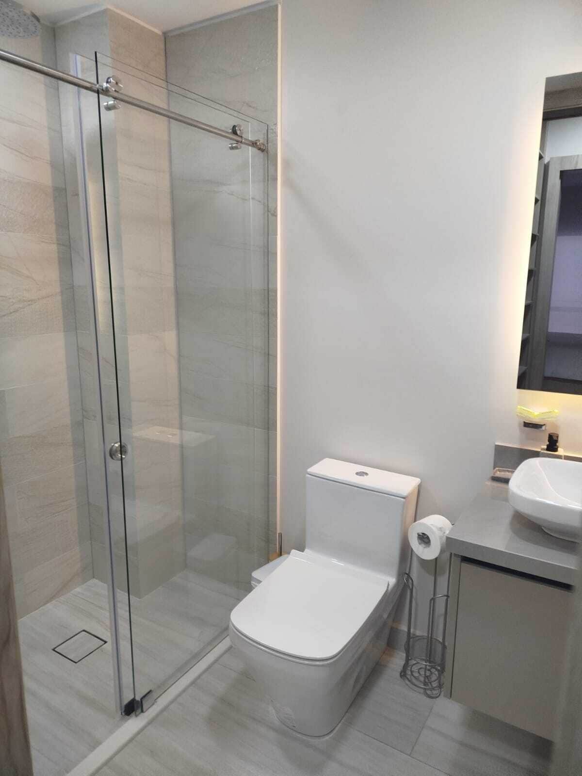 A modern bathroom with a glass-enclosed shower, a toilet, and a sink.