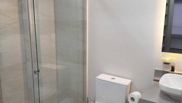 Un baño moderno con cabina de ducha de vidrio, inodoro y lavamanos.