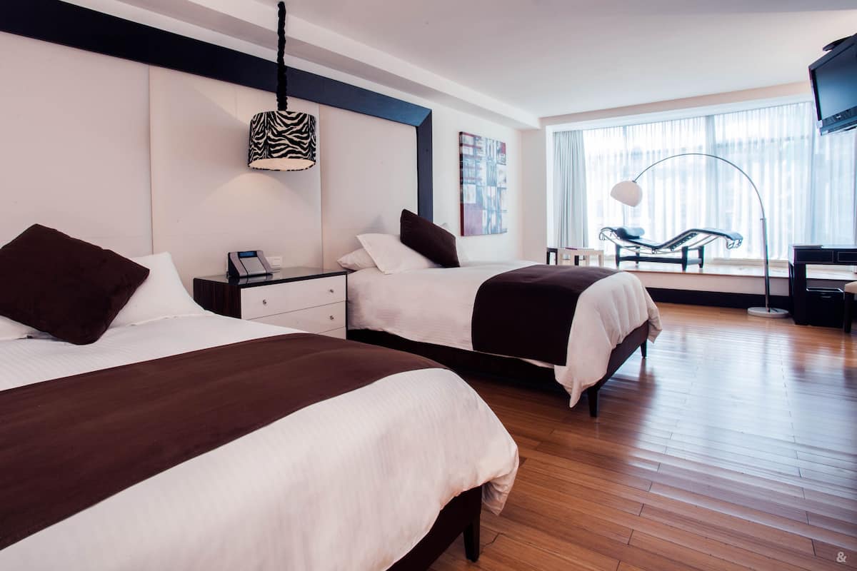 Habitación de hotel con dos camas, un escritorio, una silla y un ventanal con vistas.