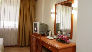 Habitación de hotel con un escritorio de madera, televisión, espejo y un ramillete de flores.