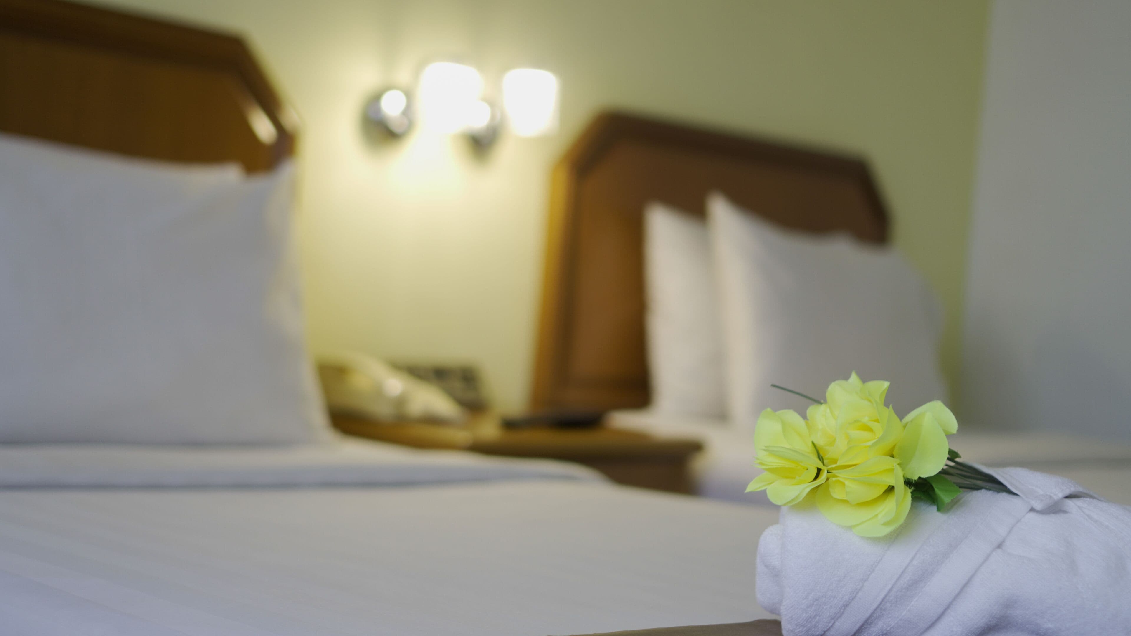 Habitación de hotel con una cama bien hecha, una mesita de noche con lámpara y un ramo de flores sobre la cama.