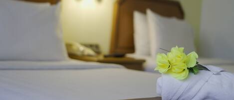 Habitación de hotel con una cama bien hecha, una mesita de noche con lámpara y un ramo de flores sobre la cama.