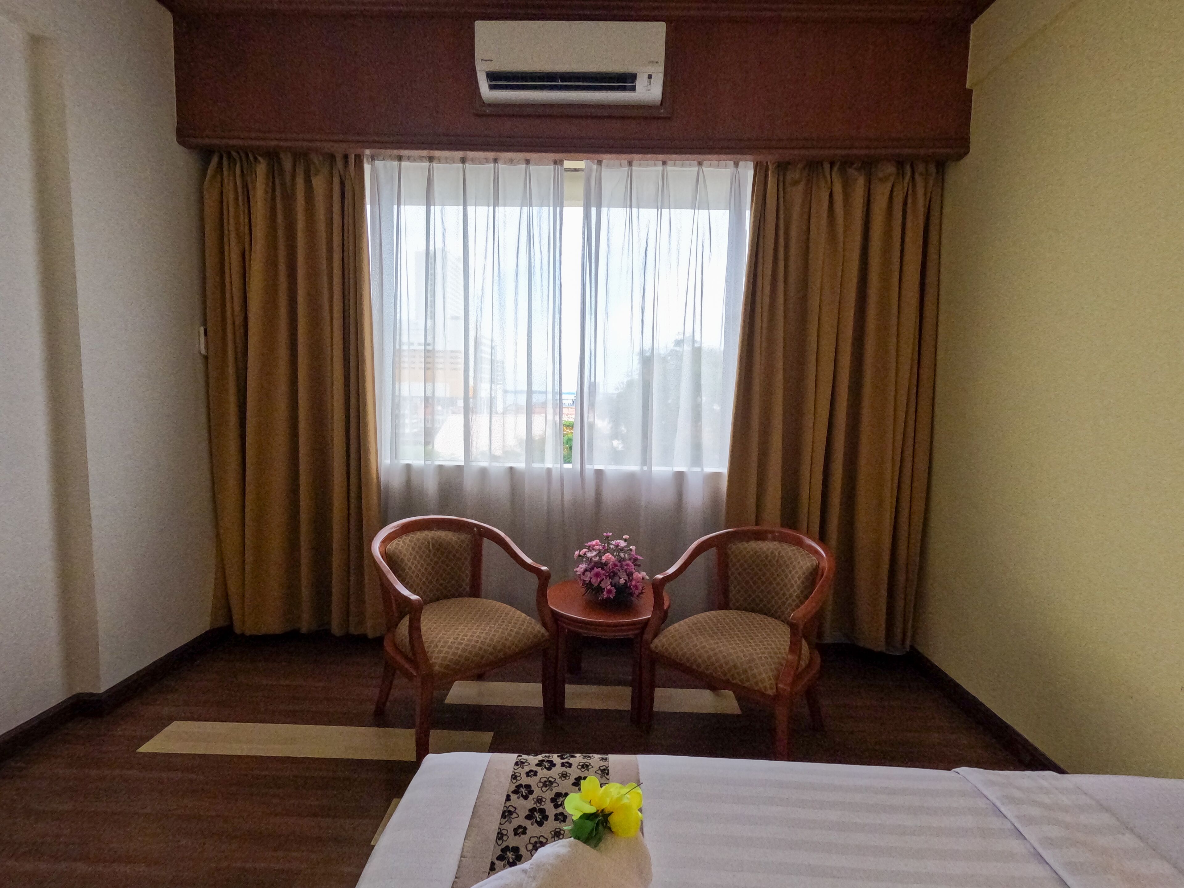 A hotel room with a bed, two chairs, a small table with a vase of flowers, and a window with curtains.