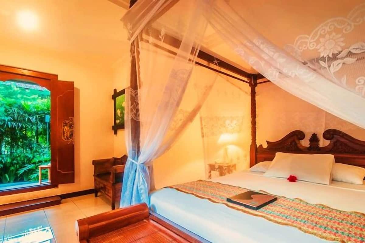 A room with a bed, a nightstand, a window with a view of greenery, and a decorative canopy.