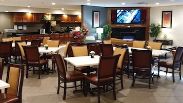 Un restaurante con varias mesas y sillas, una zona de cocina y un televisor colgado en la pared.