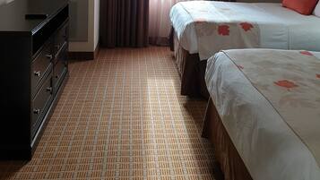 A hotel room with two beds, a dresser, a TV, and a window with curtains.