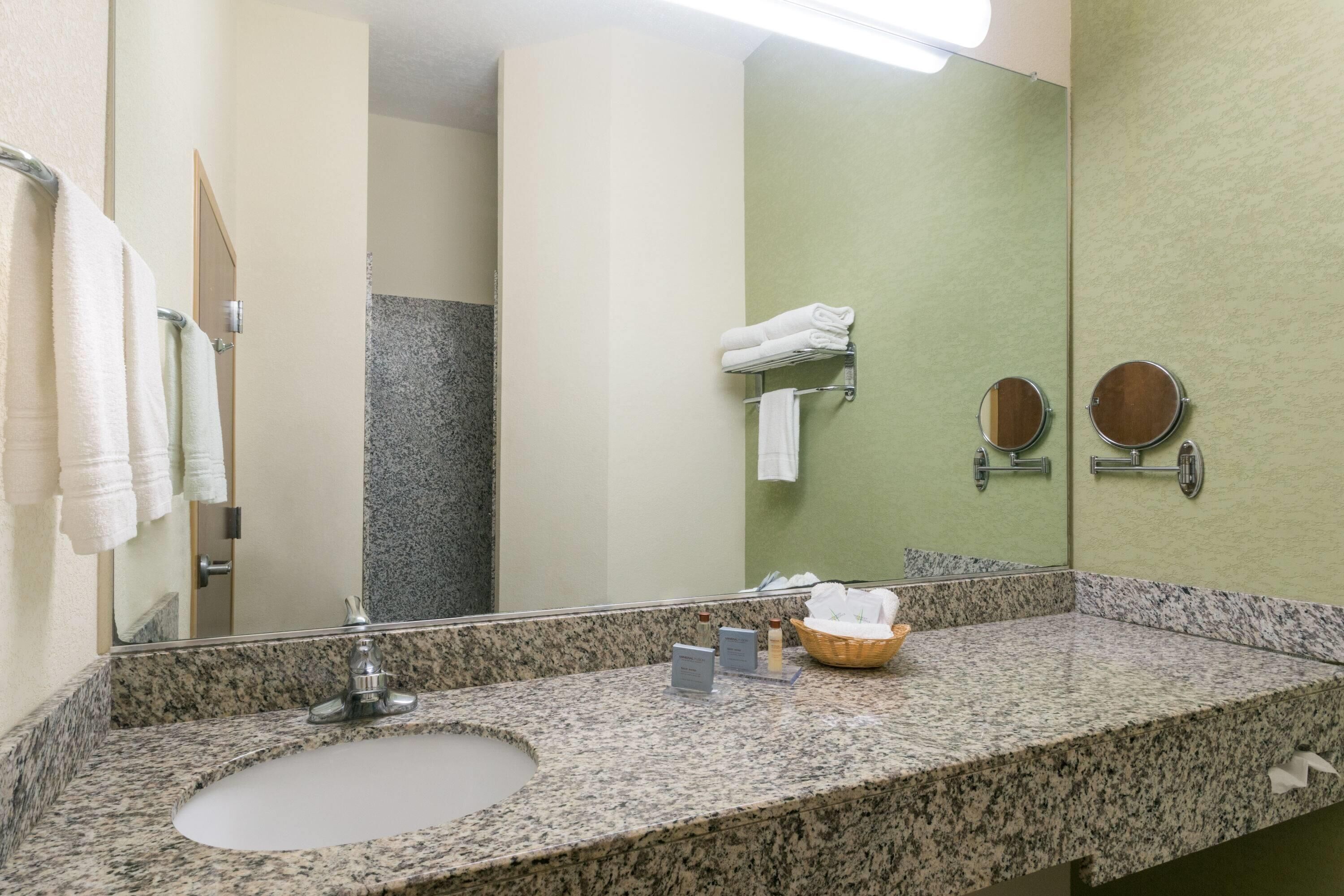 Une salle de bain avec un lavabo doté d’un plan en granit, un grand miroir et un porte-serviettes.