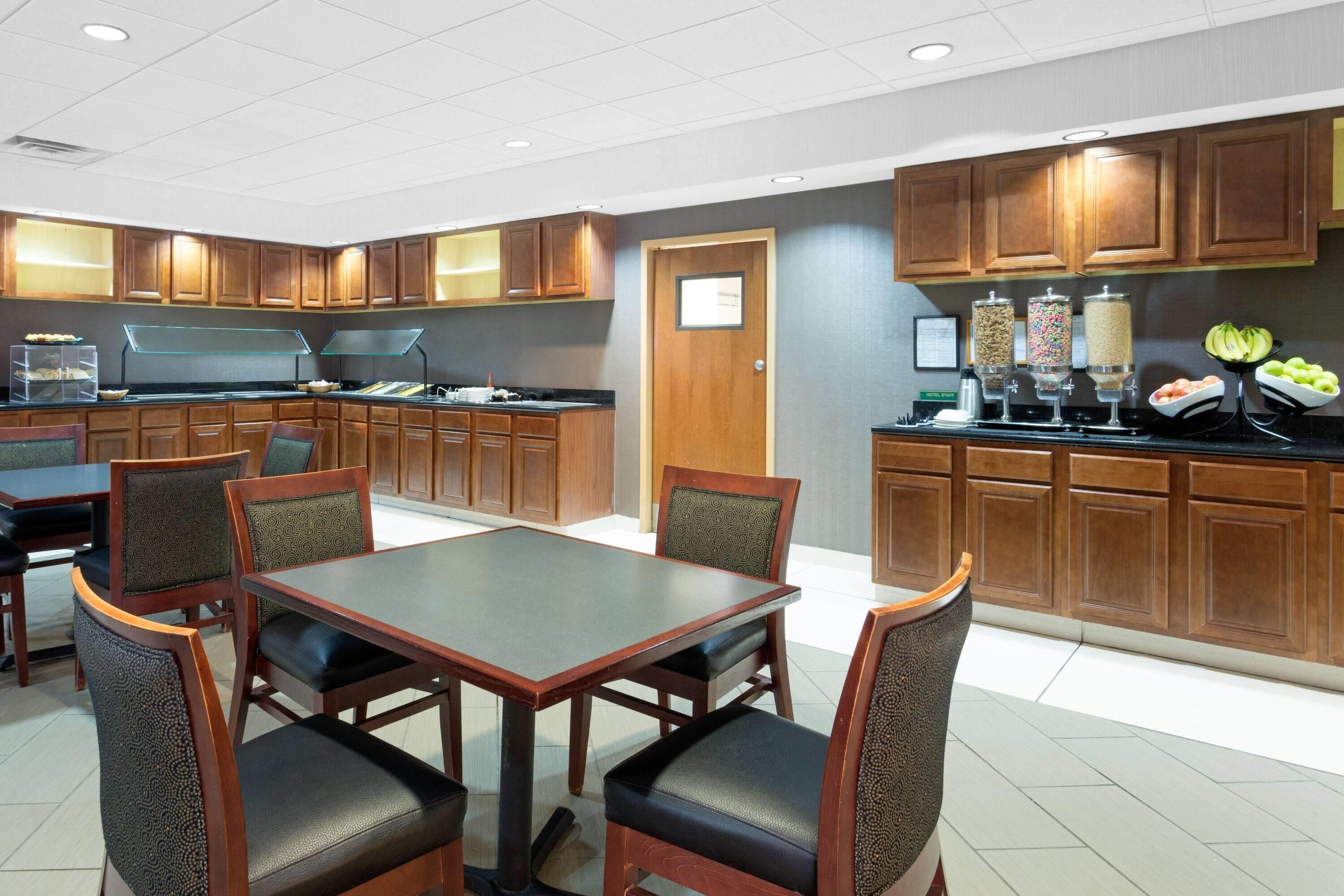 Een restaurantgedeelte in een hotel met een buffetopstelling, houten meubels en een keuken op de achtergrond.