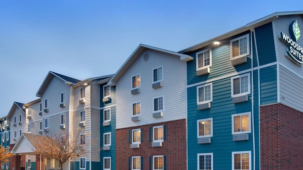 A multi-story hotel with a modern design, featuring a mix of brick and siding exteriors, and a visible sign for Woodspree Suites. - WoodSpring Suites Ankeny Des Moines (Ankeny)
