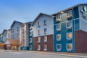 A multi-story hotel with a modern design, featuring a mix of brick and siding exteriors, and a visible sign for Woodspree Suites. - WoodSpring Suites Ankeny Des Moines (Ankeny)
