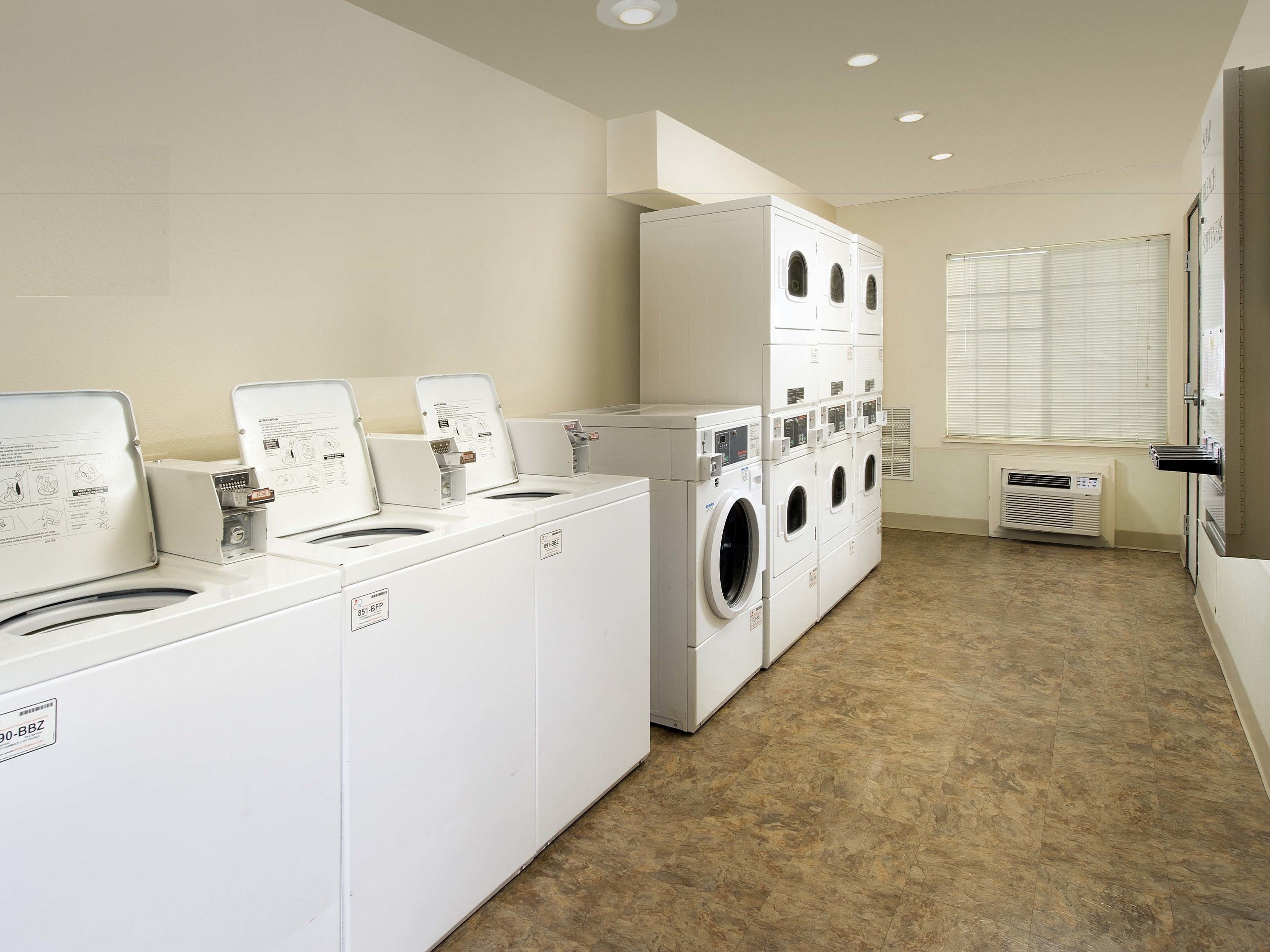A laundry room with multiple washing machines and dryers, a vent, and a window with blinds.