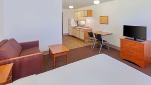 A hotel room with a bed, a small desk, a television, a sofa, and a kitchenette. - WoodSpring Suites Ankeny Des Moines (Ankeny)