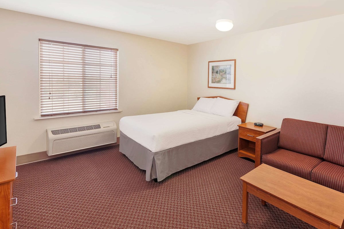 Habitación de hotel con cama, sofá, mesita, calefactor y ventana con persianas.