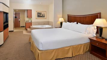 Habitación de hotel con una cama grande, dos lámparas de noche, cabecera de madera, baño con bañera y una zona de kitchenette.