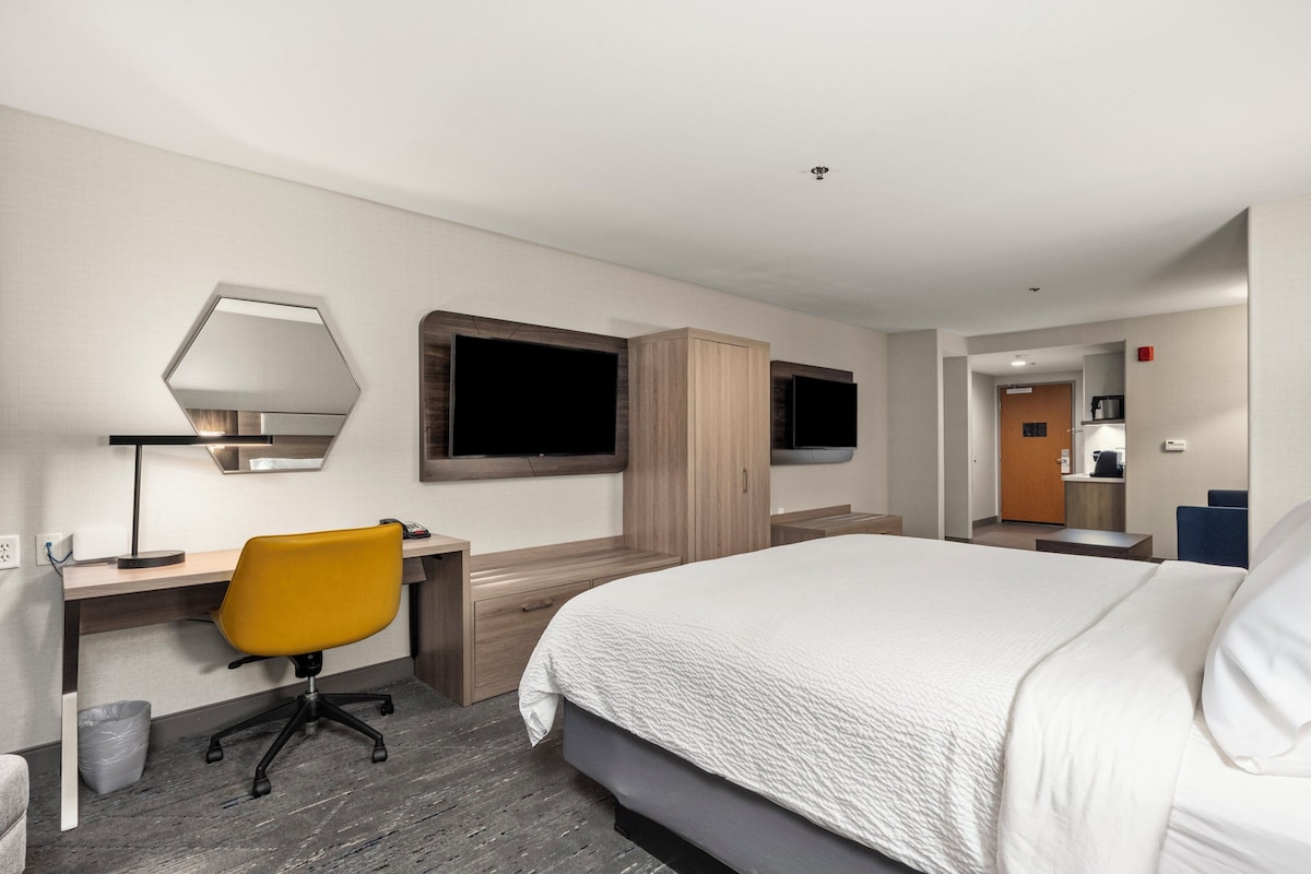 A modern hotel room with a large bed, a desk with a chair, a TV, and a wardrobe.