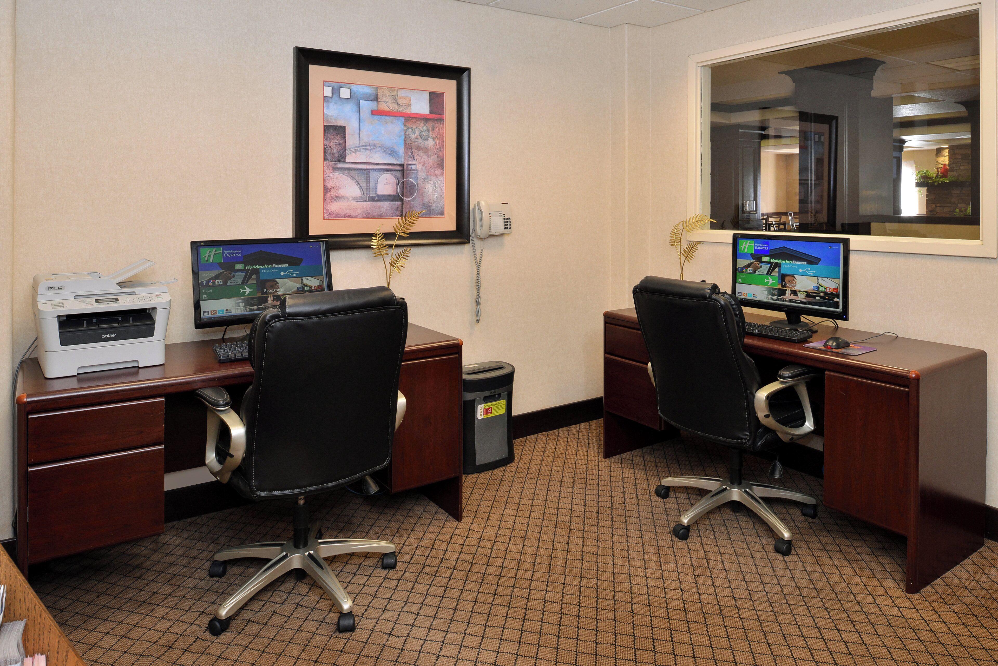 A hotel office with two desks, computers, a printer, and a framed picture on the wall.