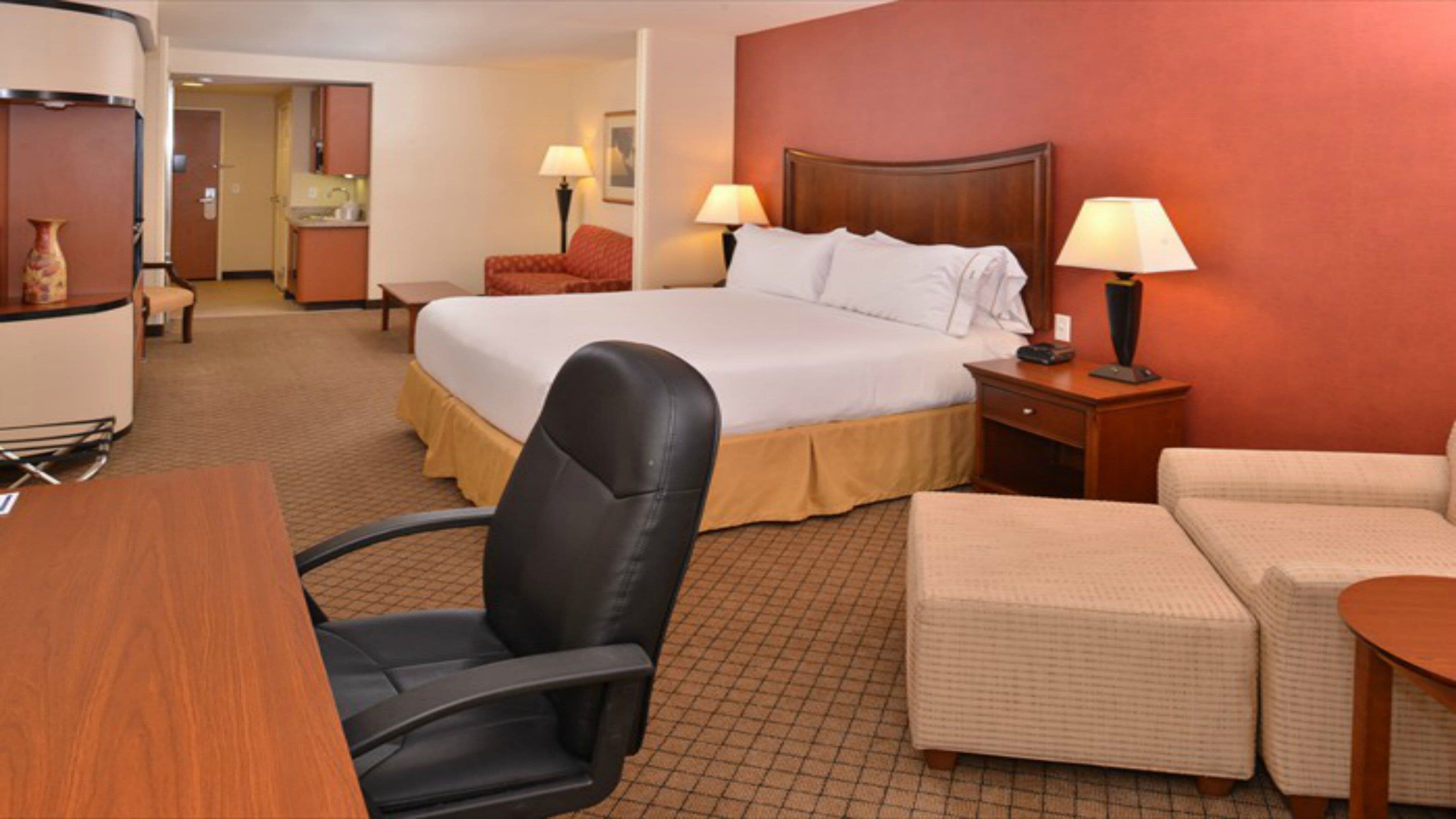 A hotel room with a bed, a desk, a chair, a sofa, and a lamp.