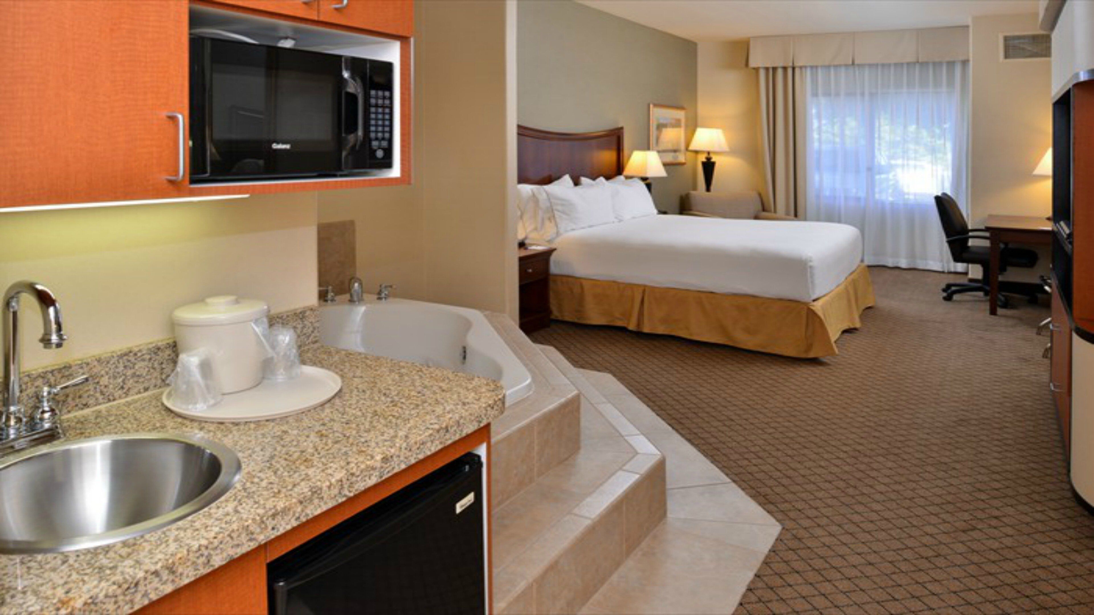 A hotel room with a kitchenette, a bed, a desk, and a bathroom.