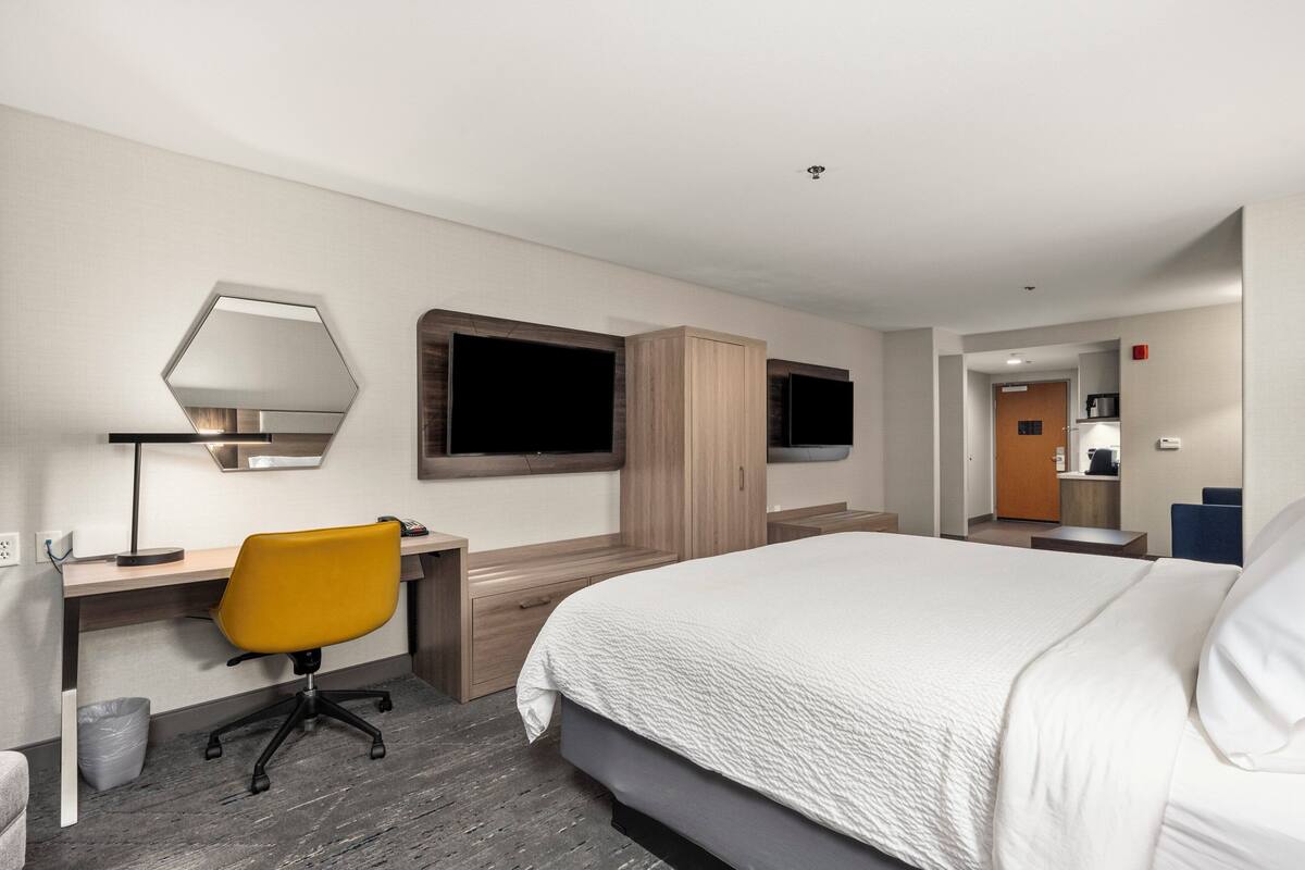 A modern hotel room with a large bed, a desk with a chair, a TV, and a wardrobe.