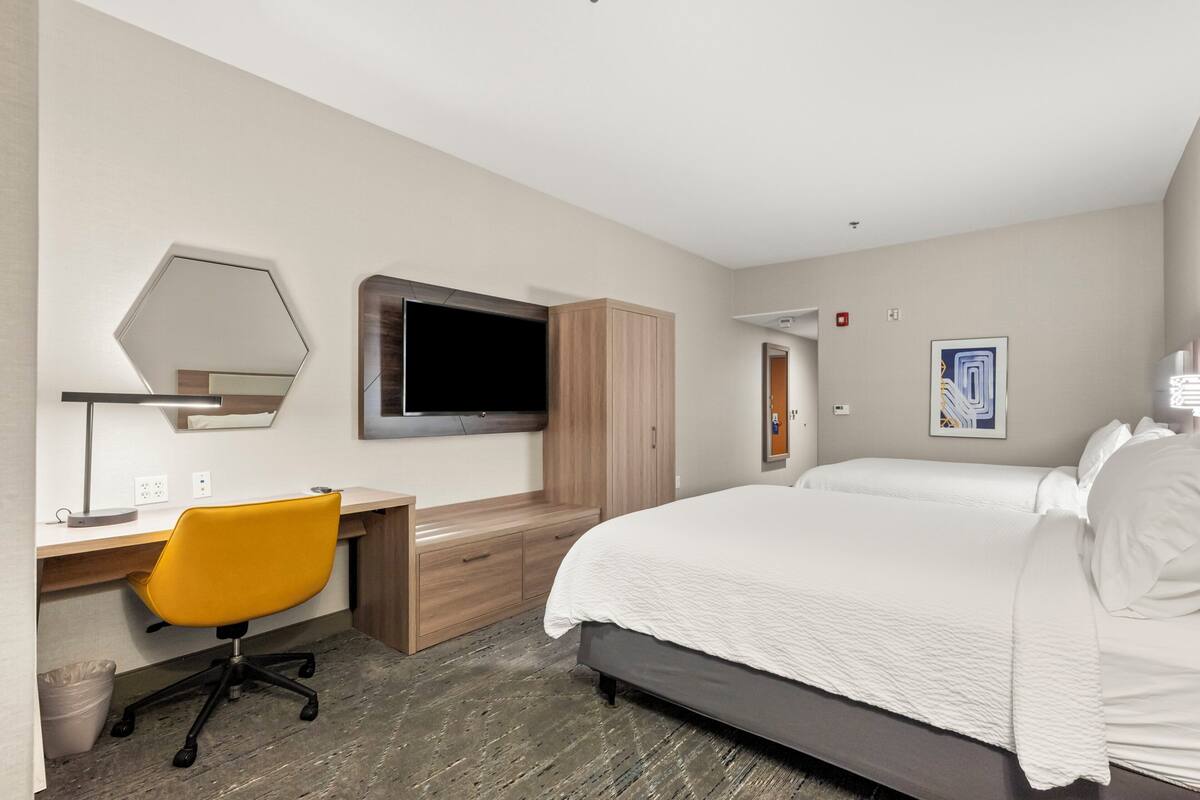 A hotel room with a bed, a desk with a chair, a TV, and a wardrobe.
