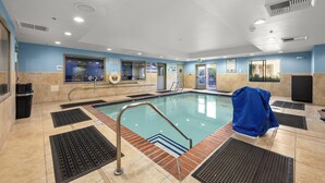 Una piscina interior con agua cristalina, suelo de baldosas y una cubierta azul en un lateral.