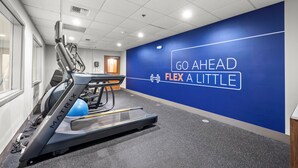 Un gimnasio con cinta de correr, bicicleta estática y pared azul con texto motivacional.