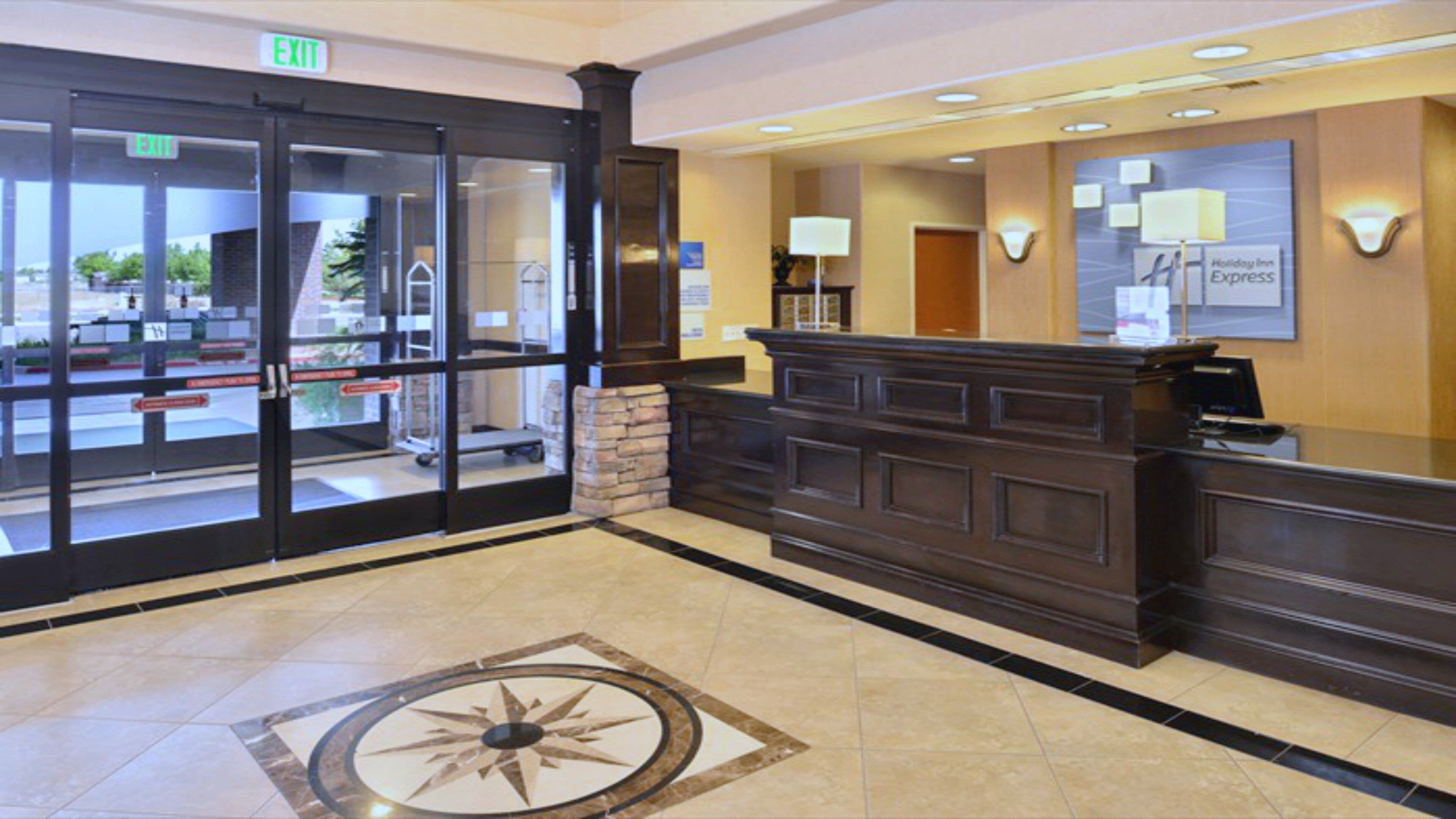 A hotel reception area with a glass door entrance, a reception desk, and a floor with a geometric design.