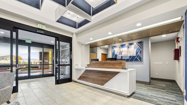 Zona de recepción con puerta de vidrio, mostrador de recepción y pared con diseño geométrico.