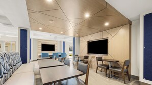 Un comedor moderno con mesas y sillas largas, un televisor de pantalla plana grande montado en la pared y un diseño de pared con motivos.