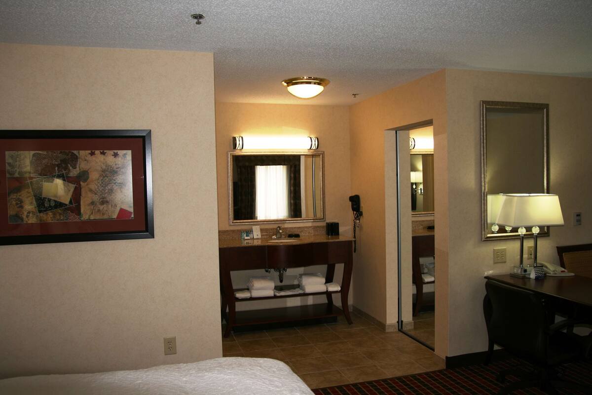 A hotel room with a bed, a bathroom with a sink and mirror, and a desk with a lamp.