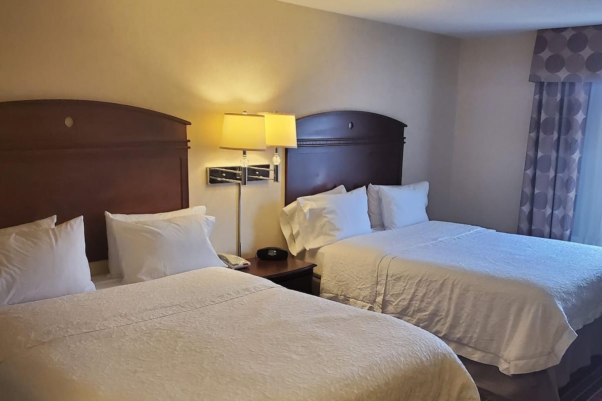 A hotel room with two beds, a nightstand with a lamp, and a ceiling light.