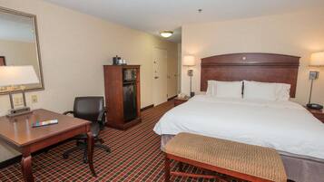 A hotel room with a large bed, a desk, a chair, a small cabinet, and a bench.