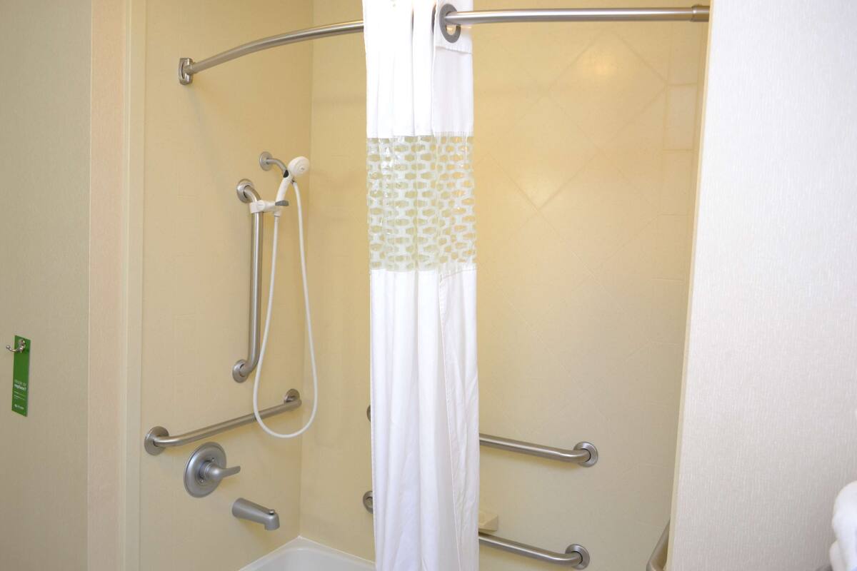 A shower area with a white shower curtain, grab bars, and a handheld showerhead.