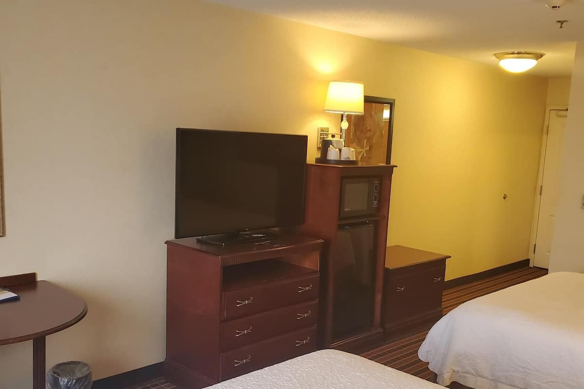 A hotel room with two beds, a TV, a desk with a lamp, and a small kitchenette.