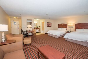 A hotel room with two beds, a desk, a chair, and a small table.