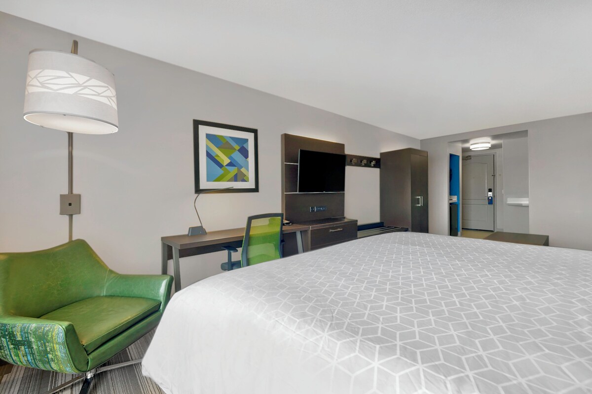 A hotel room with a large bed, a desk with a chair, a television, and a lamp.