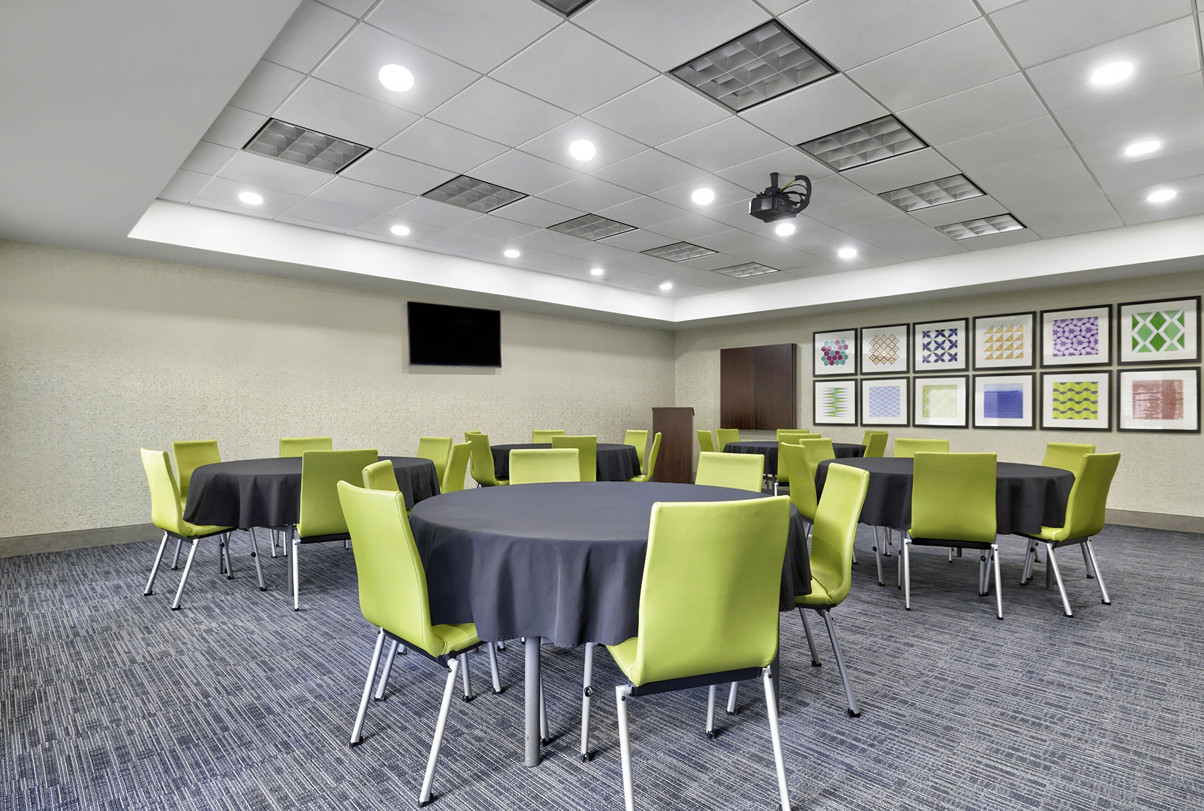 A conference room with round tables, green chairs, and a projector on the ceiling.